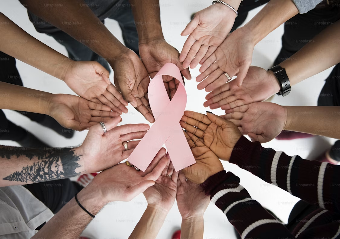 Hands gathered around a cancer awareness ribbon